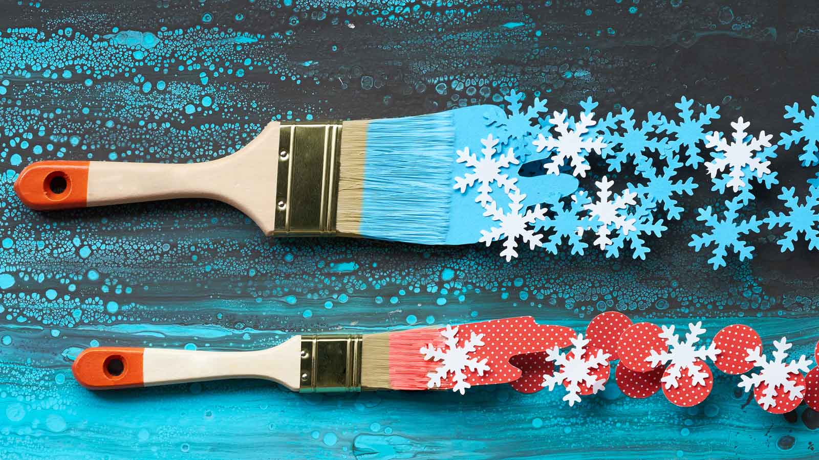 Two paint brushes painting snowflakes across a teal background