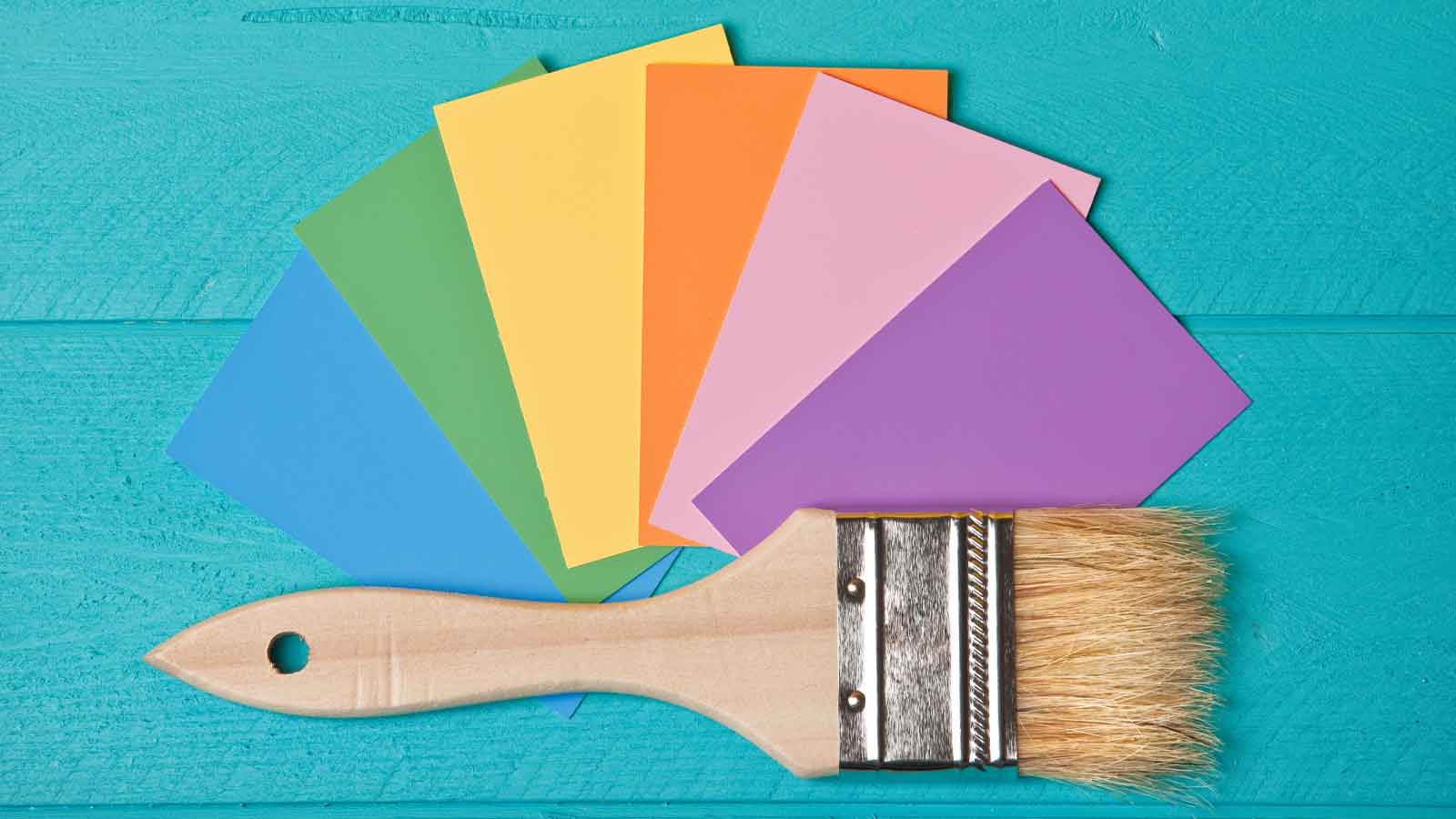 Paint brush sitting on top of a group of color cards on a wooden teal background