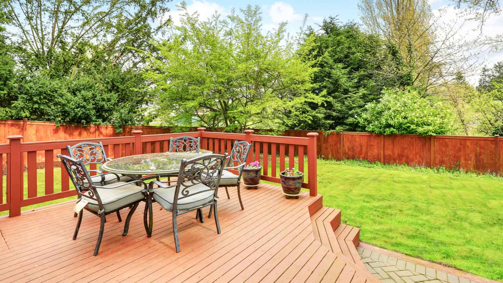 Backyard deck with table up on the deck with a lush green lawn in the distance.