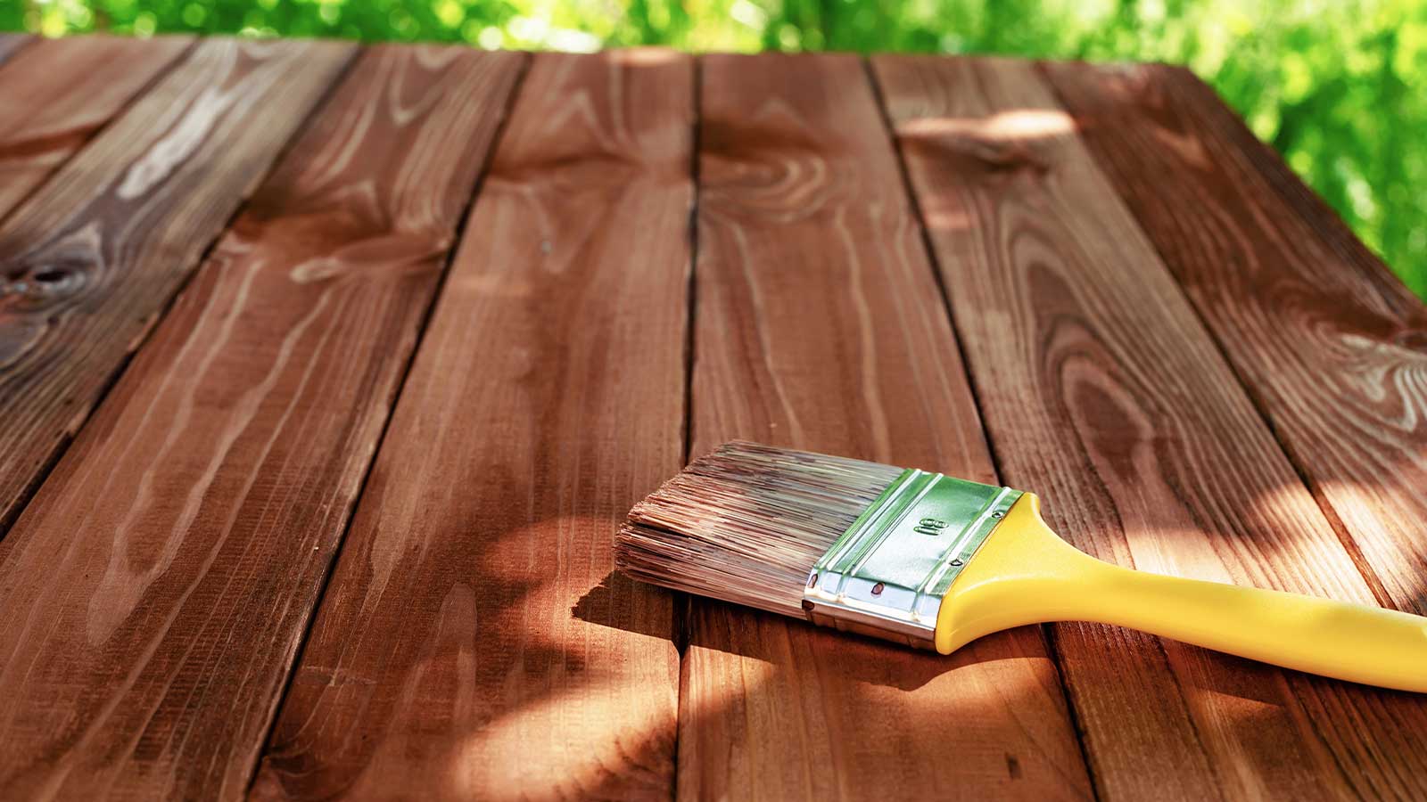 Close-up view of a wooden deck being stained with a yellow-handled brush under natural light, illustrating the precise care involved in professional deck staining in Vancouver homes.