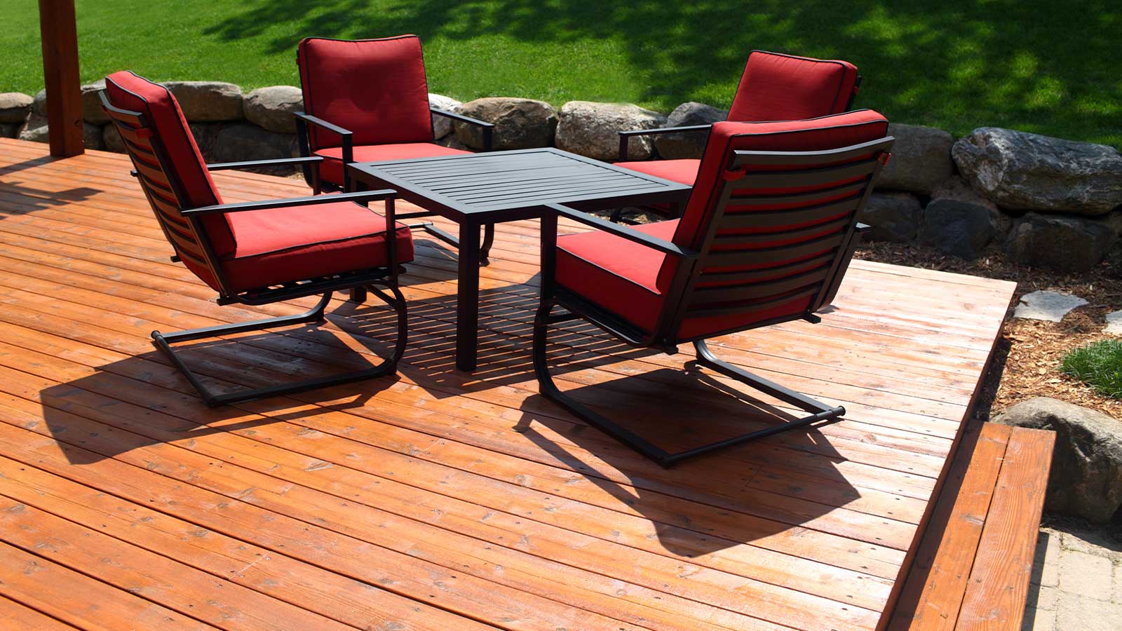 Freshly stained wooden deck with modern red patio chairs and black metal table under daylight, a perfect example of a stylish and weather-resistant finish from deck staining in Vancouver.