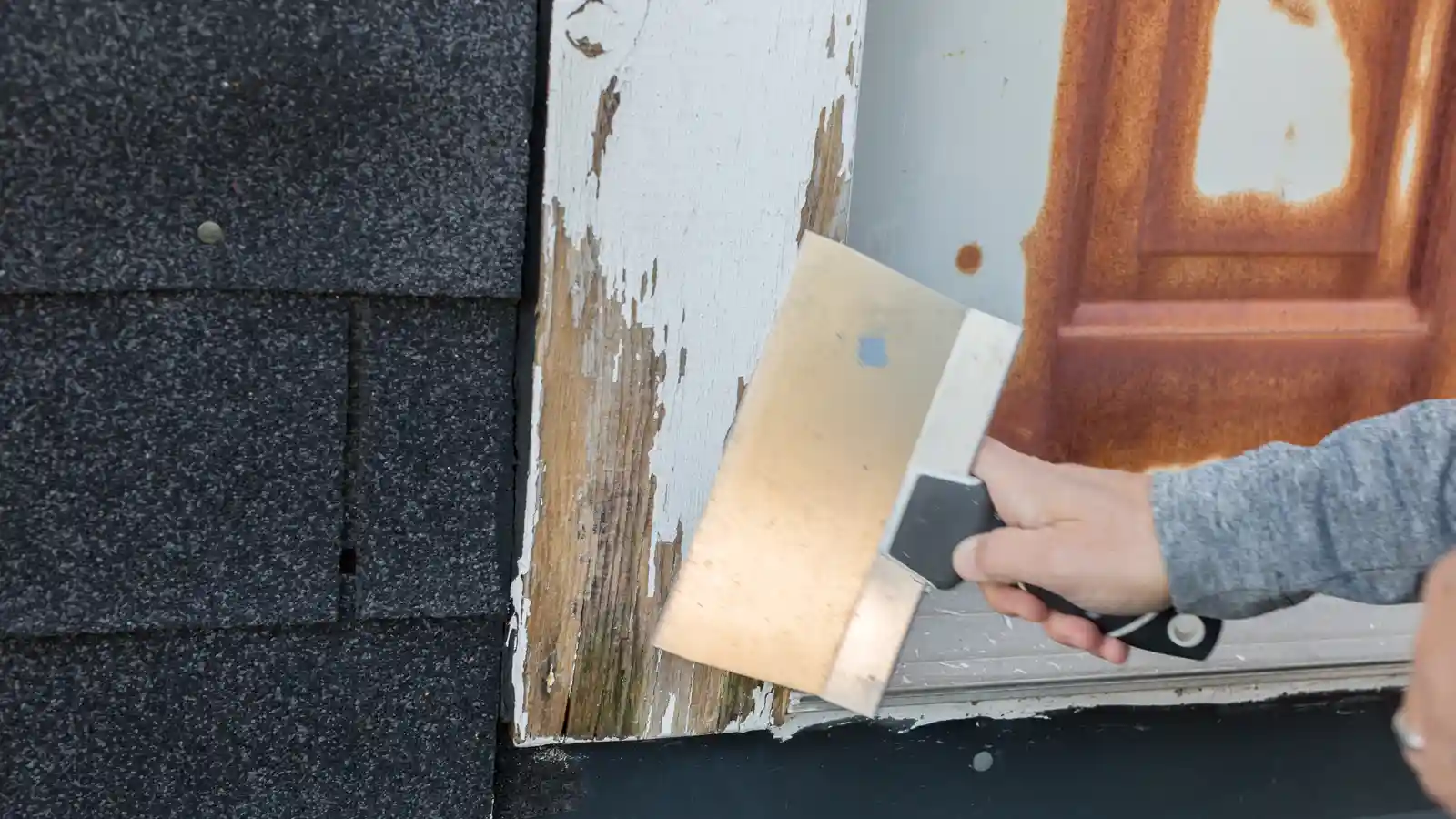 Cropped image of a man taking the old paint off a wood frame so he can apply new paint to the area.