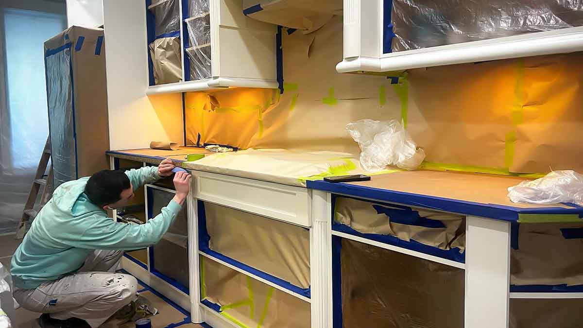 Crew member for Roarty Painting applying tape lines to mask kitchen cabinets