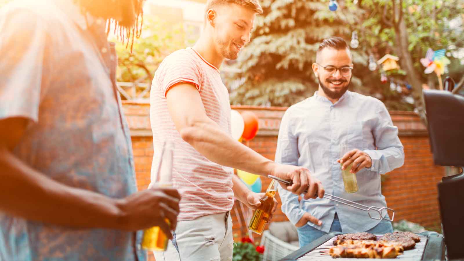 Men grilling on bbq at barbecue party at backyard. Selective focus to blond man smiling while grilling. They are having fun ad patio party.