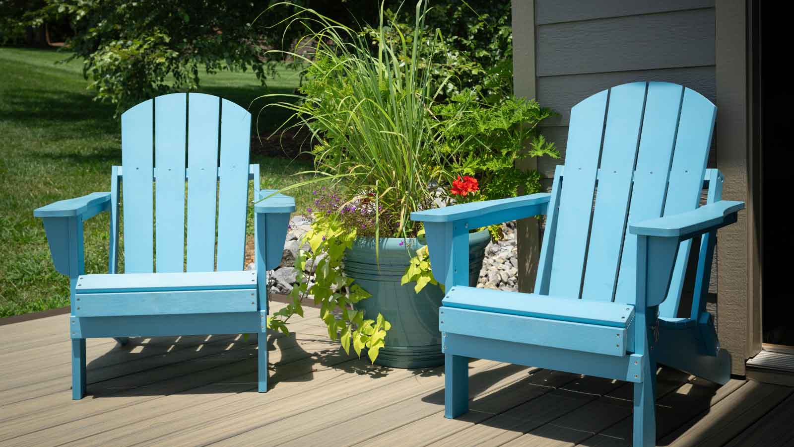 Deck Stain Langley Two empty, turquoise, blue Adirondack chairs on a deck, patio, dock or porch with a container of potted plants and flowers.